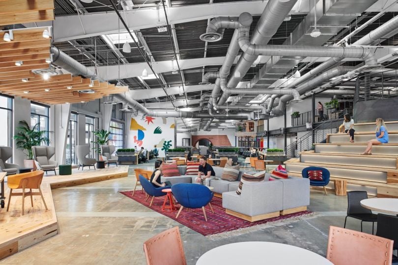 Favor Delivery office space. Stadium seating can be seen to the right while a homey open concept work and collaboration space is the focus of the photo. People are scattered around chatting.